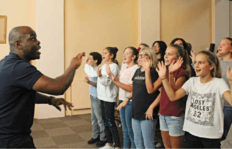 Comment êtes-vous devenu chef de la chorale des Gospel Kids ? J’ai découvert le gospel à 17 ans, en 2000, en passant un jour devant l’église de Hautepierre, quartier où j’habitais. J’ai entendu Oh happy day qui est chanté dans Sister Act 2, film qui m’avait fortement marqué. À ce moment-là, il est devenu évident pour moi que j’allais rejoindre le groupe. J’ai mis de côté ce que j’aimais pour me consacrer entièrement à la chorale des High Rock Gospel Singers, créée et dirigée par le pasteur Frédéric Setodzo, qui a été super avec moi et m’a encouragé. Je n’avais pas la fibre d’un chanteur mais je crois que, avec de l’énergie, de la volonté et du plaisir, on peut faire beaucoup. En 2003, j’ai commencé à intervenir bénévolement dans des écoles. Je me sentais comme un vrai professeur et j’aimais, déjà à l’époque, beaucoup travailler avec les enfants. À la kermesse de fin d’année, j’ai ressenti l’enthousiasme des enfants et le plaisir des enseignants et des parents. J’ai laissé tomber mon travail dans un garage où je ne me sentais pas à ma place et j’ai fait des petits boulots à côté. C’est avec ma femme Flora, que j’ai rencontrée aux High Rock Gospel Singers, que j’ai créé les Gospel Kids en 2004. Que représente le gospel pour vous ? Au moment où j’ai découvert le gospel, j’ai senti que cela m’apporterait tout ce que j’avais espéré. À travers lui, on chante l’amour, la tolérance, le respect, le partage. J’étais un ado un peu perdu qui se posait des questions sur le sens de la vie et le bonheur. J’ai toujours aimé les chansons à message. Quand j’étais jeune, mes copains baignaient dans le rap et moi je me cachais pour écouter la comédie musicale NotreDame de Paris. Les professeurs ne croyaient pas en moi, on m’a mis dans une section d’enseignement adapté où on est en bleu de travail dans la cour et on n’est pas mélangé avec le reste des élèves. J’ai passé un CAP de mécanicien poids lourds, puis j’ai laissé tomber le BEP en cours. À partir du moment où j’ai commencé à chanter du gospel, des gens ont cru en moi. Quelles valeurs voulez-vous transmettre ? Beaucoup de jeunes ne se rendent pas compte de leur potentiel, dans tous les domaines de la vie. Il n’y a pas d’audition pour intégrer la chorale car je vois la marge de progrès dans les imperfections et je veux que les enfants prennent du plaisir, pas qu’ils soient rabaissés, comme j’ai pu l’être. Je donne beaucoup d’encouragement et veille particulièrement aux plus motivés et qui veulent progresser. Certains sont bluffants ! Que vous apporte votre foi dans ce travail ? J’ai un lien très fort avec l’Église et la prière est importante pour moi. Avec mes parents et mes cinq frères et sœurs, dont je suis l’aîné, nous allions tous les dimanches au culte et j’ai réussi à partager cela avec ma femme et à le transmettre à mes enfants. En 2001, j’ai effectué un voyage avec les High Rock Gospel Singers au Cameroun qui m’a donné une foi incroyable. J’y ai vu des gens qui ne vivaient que par leur foi. C’est là-bas que des personnes m’ont dit que j’avais un don et que le Seigneur m’appelait. J’ai toujours gardé cette voix en moi qui me disait que j’allais réussir quelque chose. Je suis aujourd’hui quelqu’un qui doute peu et qui n’a pas peur. Je pense que Dieu fait bien les choses et qu’on peut renverser les situations lorsque viennent les difficultés, en s’appuyant sur les gens qui vous aident.