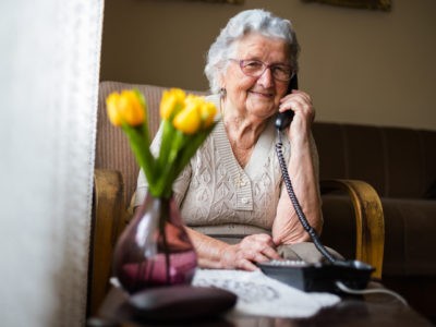 Une dame âgée est au téléphone avec en avant-plan des tulipes jaunes dans un vase