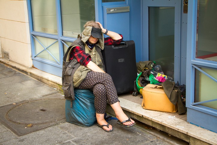 Une femme sans domicile fixe avec des sacs et une valise sur un trottoir à Paris
