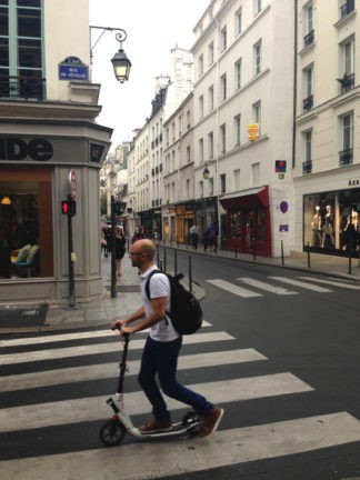 Un homme sur une trottinette sur un passage piéton à Paris