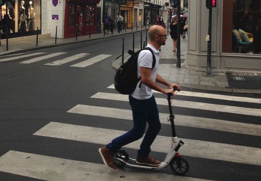 Un homme sur une trottinette sur un passage piéton à Paris